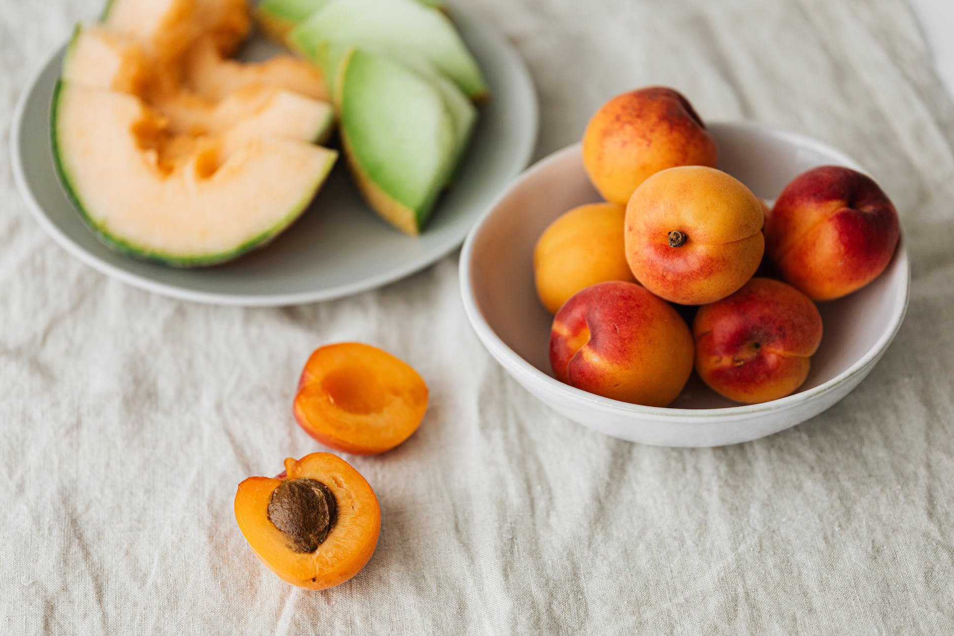 ripe healthy apricots in bowl near plate with various melons